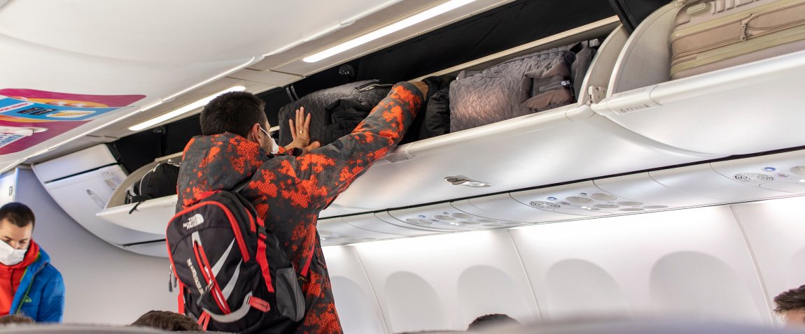 man in on board the plane puts luggage on the shelf